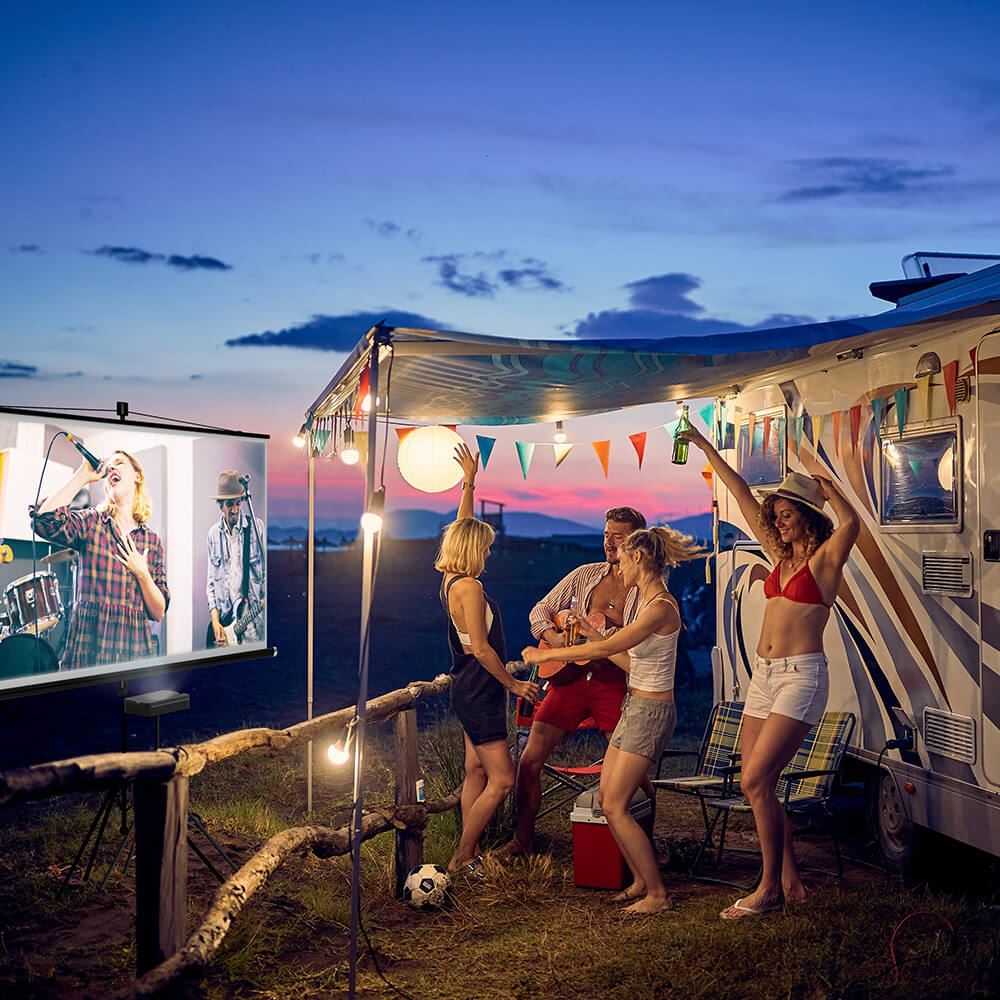 Group of friends enjoying outdoor entertainment beside a camper van, watching music videos on a portable projector at sunset — mobile lifestyle with on-the-go streaming and gaming.